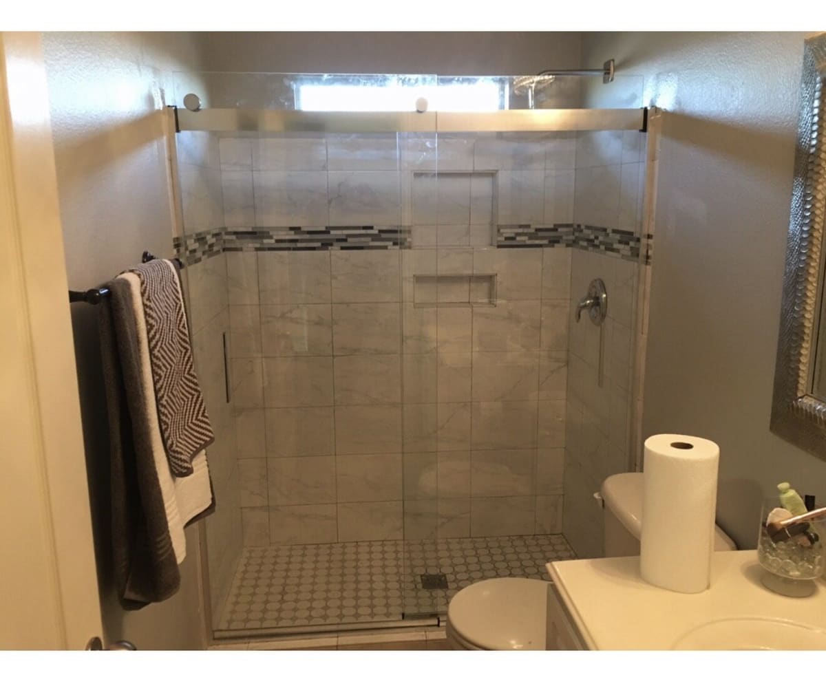 Marble tile walk-in shower with sliding glass door and mosaic accent band